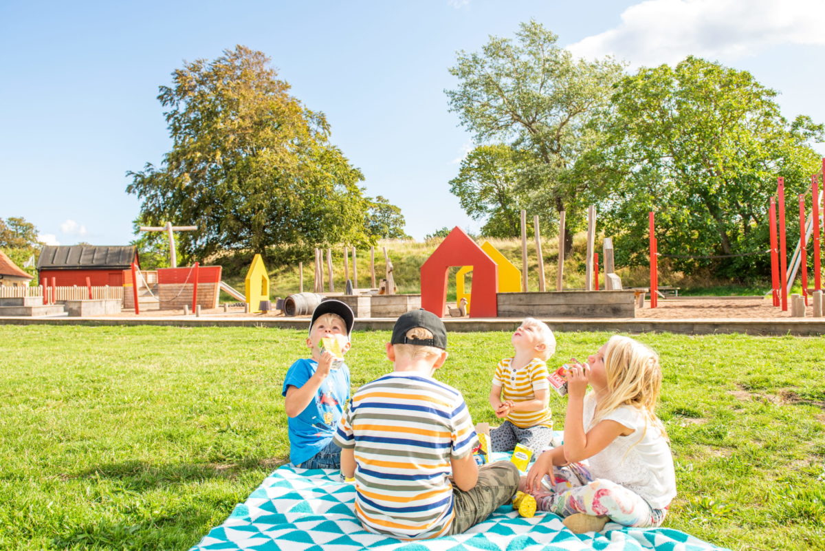 Fyra barn sitter på en filt och äter picknick.