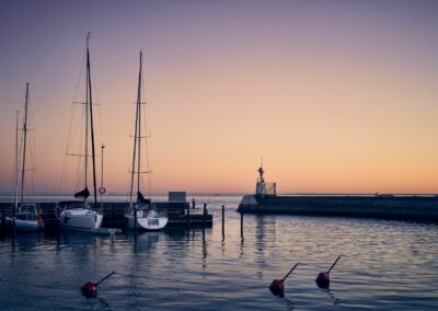 Tre segelbåtar ligger i en hamn. Det är solnedgång