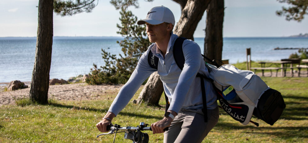 Christian Hovstadius cyklar med en golfbag över axeln