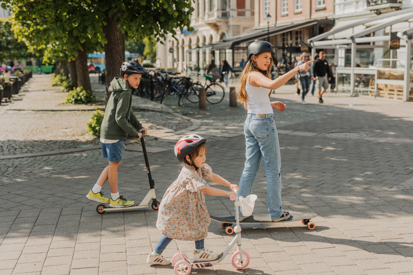 Tre barn åker kickbike och skateboard