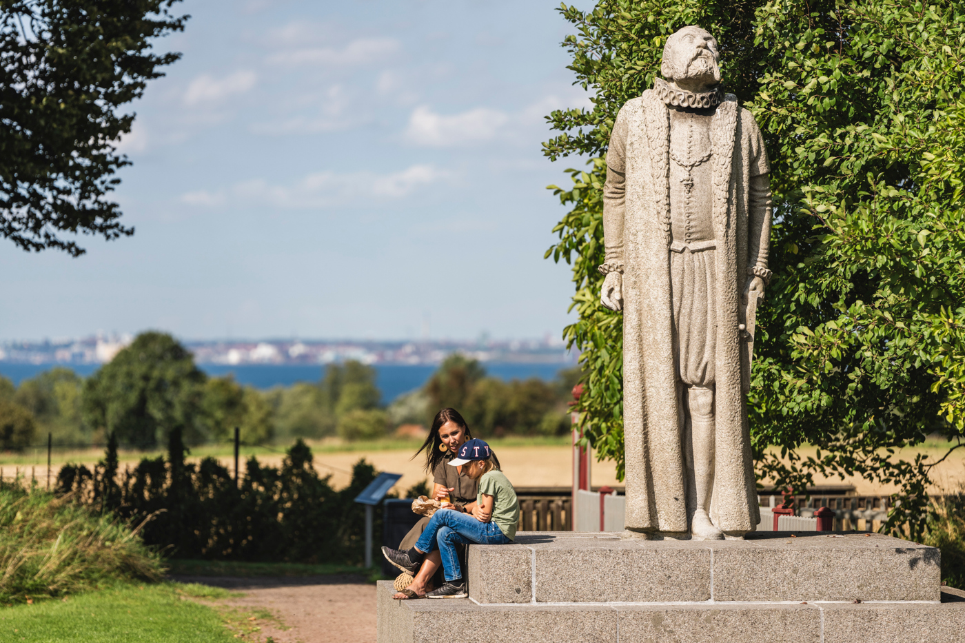 en kvinna och ett barn sitter intill tycho brahe statyn