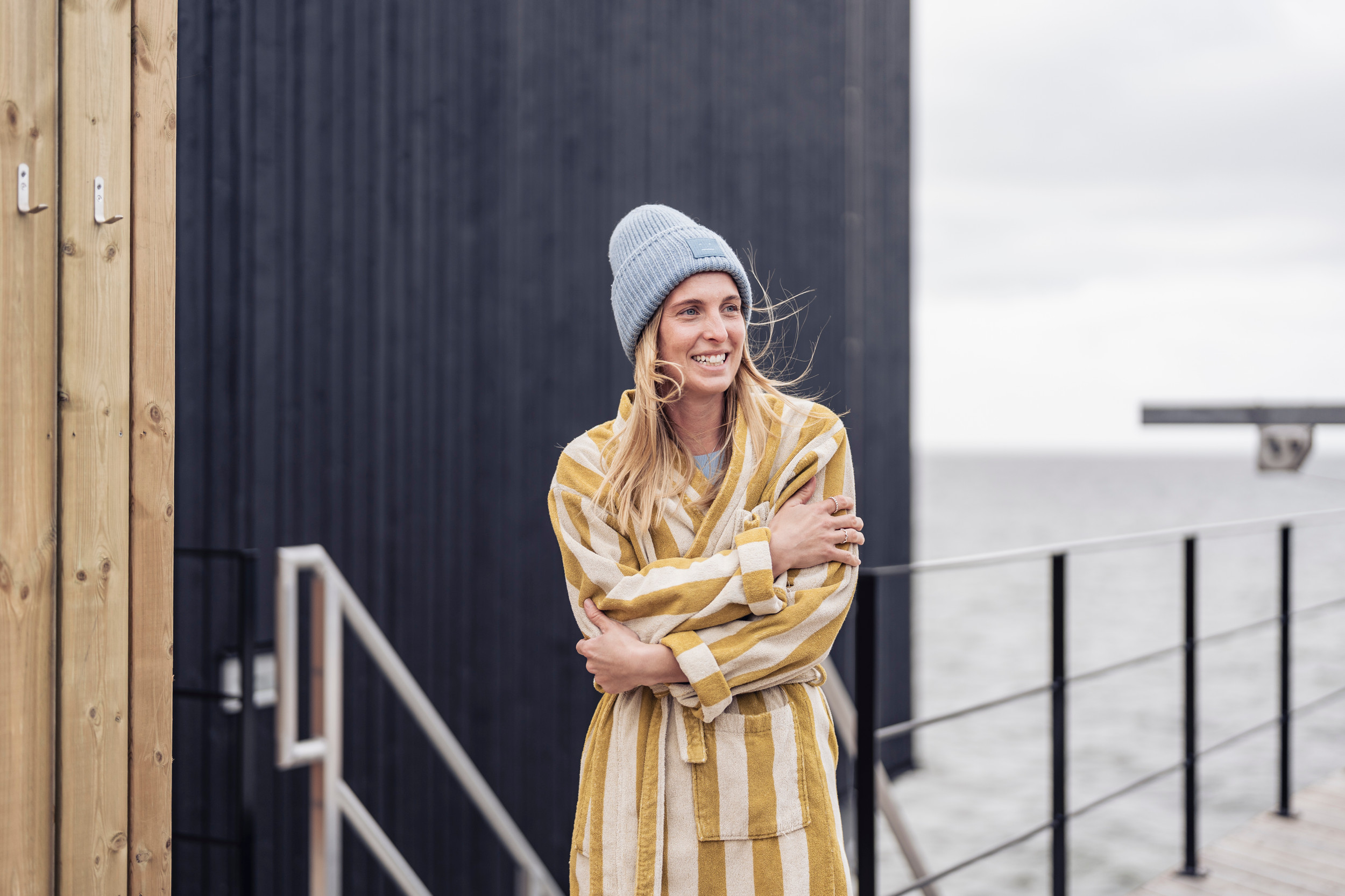 En kvinna klädd i badrock och mössa står vid Landskronas kallbadhus